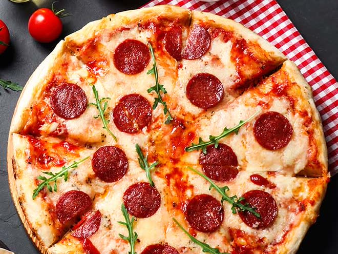 Een pizza met pepperoni, mozzarella en rucola, in punten gesneden, op een rood-wit geruite doek.